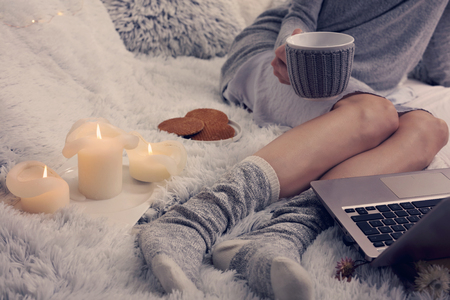 Cozy evening , warm woolen socks, soft blanket, candles. Woman relaxing at home,drinking cacao, using laptop. Comfy lifestyle.の写真素材