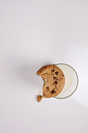 Chocolate chip cookie with Bite Eaten and glass of milk on white background, minimalism concept. New year and christmas holiday background, copy spaceの写真素材