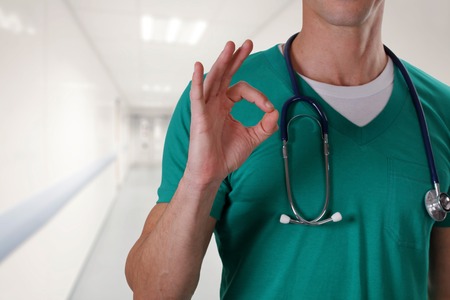 Portrait an unknown male doctor with a stethoscope showing thumb up in hospital hallway. Health care and medical concept.の写真素材