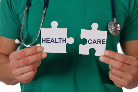 Health care. Doctor holding two pieces of a puzzle isolated on white background.の写真素材