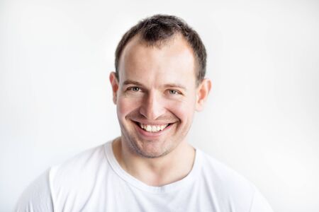 Closeup portrait of smiling 30 years old caucasian white man on white background in white t-shirt. Confident happy smart modern man. Lifestyle. Wide smile with healthy teethの写真素材