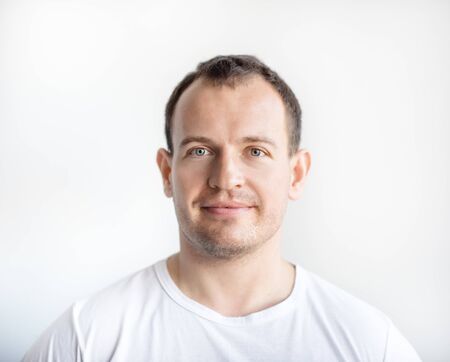 Closeup portrait of serious 30 years old caucasian white man on white background in white t-shirt. Confident happy smart modern man looking in camera. Lifestyle.の写真素材
