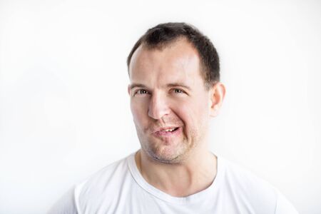 Closeup portrait of disgusted 30 years old caucasian white man on white background in white t-shirt. Man making weird face and looking in camera. Afraid, desperate, disgusted guy conceptual pictureの写真素材