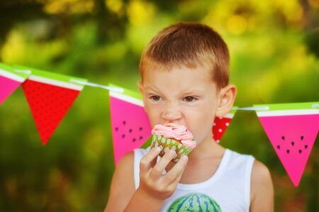 5 years old boy eat homemade gluten free healthy cupcake. Organic natural baking for children. Delicious muffin on birthday party. Children on outdoors birthday party in summer time. Hungry kid.の写真素材