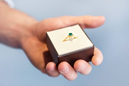 Cropped close-up of man hand holding jewelry box with engagement diamond and emerald ring. Beautiful...