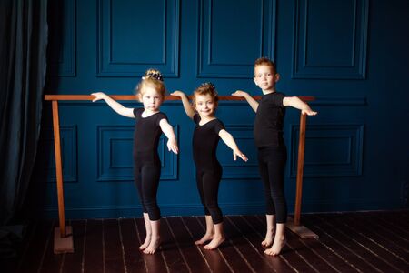 Portrait of 3 little children two girls ballerina and small boy dancer in black leotard practicing at ballet barre at dance studio. Kids hobby dancing. Active lifestyle in childhood.の写真素材