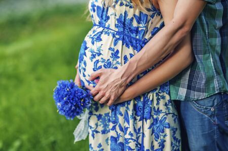 Happy and young pregnant couple hugging in nature with bouquet of knapweeds in hands. Detail of young pregnant couple. New Familyの写真素材