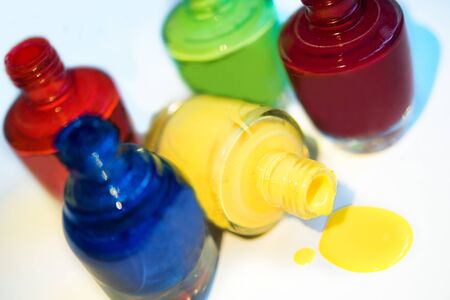 Close up of 5 open bottles of nail polish blue, red, dark red, green, yellow isolated on white background. Open yellow bottle lay down and splatter. Bright and colorful manicure and pedicureの写真素材
