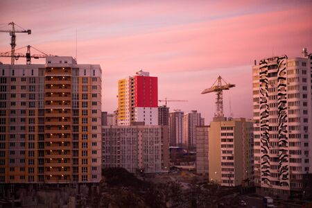 Industrial construction cranes and building silhouettes over sun at sunrise. Unfinished buildings...