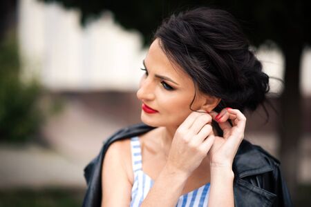 Horizontal portrait of young beautiful brunette woman with red lipstick touching her earring and...