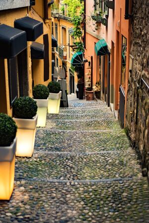 Narrow street with orange buildings and lanterns in Bellagio town at the famous Italian lake Como,...