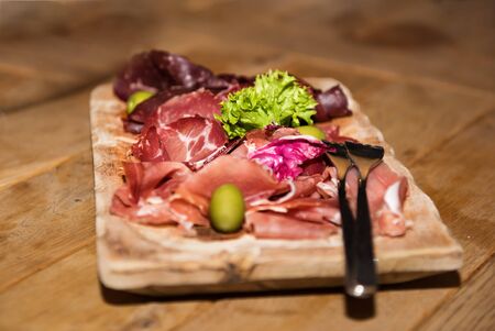 Restaurant serving of thin slices of prosciutto, jambon with olives and salad on a cutting board. Smoked tasty meat on wooden table.の写真素材