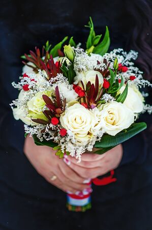 Beautiful winter colorful wedding bouquet with white roses in womans hands. Wedding decor. Idea for bridal bouquet. Flowers in womans handsの写真素材
