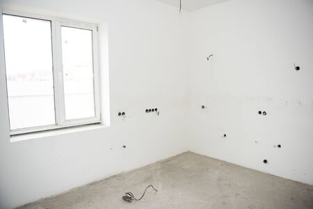 Interior construction of housing project with drywall installed and patched without painting applied, plastered walls and electrical wiring with windowの写真素材