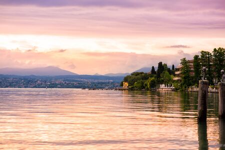 Scenic landscape of sunset with dramatic pink sky and reflection in water on Garda lake in Sirmione, Lombardy, Italy. Beautiful nature close to people. Travel tourism destination.の写真素材
