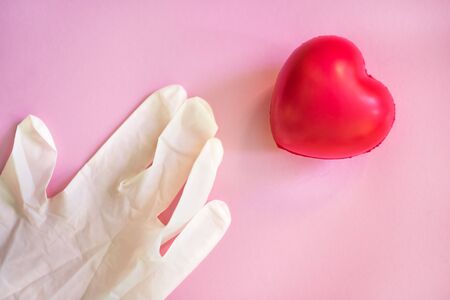 One latex protective rubber white glove on pink background with red heart nearby. Medicine health care concept. Protection from covid-2019 coronavirus. Medical concept. Medical background.の写真素材