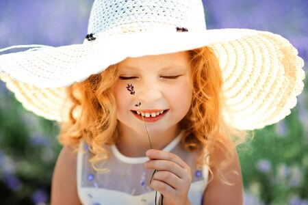 Close-up portrait of happy cute little blonde curly girl with closed eyes wearing white dress and...
