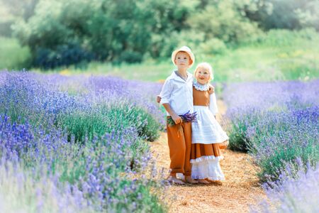 Village scene with children in vintage clothes in the middle of a lavender field. Boy in white hat, shirt and brown trousers hug beautiful girl in brown dress with white apron. Typical rural Provence.の写真素材