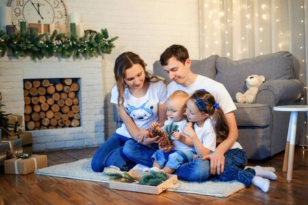 Theme Christmas and New Year family circle. Young Caucasian family with 1 year old son and 6 years old daughter sitting on floor in living room. Christmas decorations. Boy and girl kids and parents.の写真素材