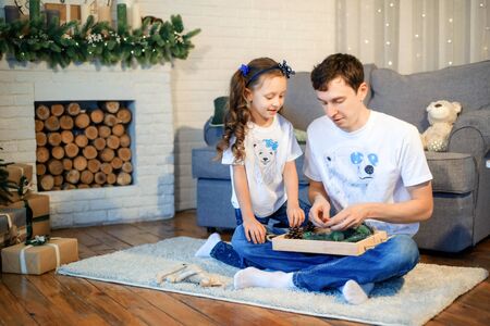 Sweet little girl together with beautiful young dad sitting on floor in living room at home in evening. Happy family concept. Love. Trust. Togetherness. Parents and children. Family time. Stay home.の写真素材