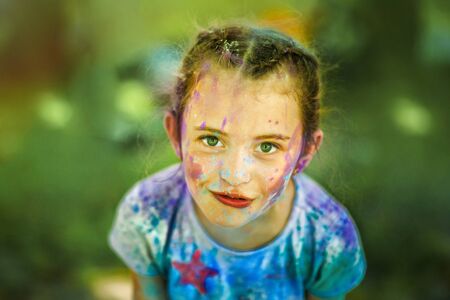 Portrait of little emotional 6 years old girl with face smeared with holi colors in sunny summer day. Concept for Indian festival Holi. Summer activity outdoors. How to spend time with childrenの写真素材