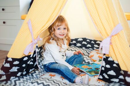 Little smiling blonde 3 years old girl play in yellow tent wigwam in her bedroom. Time to play...