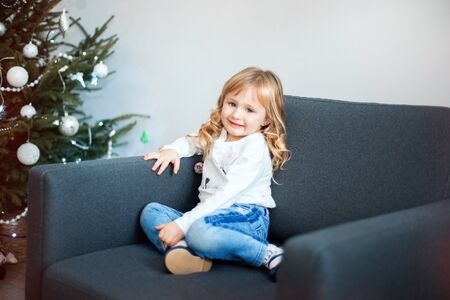 Interesting little girl sits on chair. Merry Christmas and Happy New Year. Lovely baby enjoy christmas. Childhood memories. Little child celebrate christmas at home. Family holiday.の写真素材
