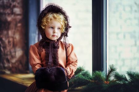 Little beautiful 4 years old curly blonde girl in brown vintage retro hat and dress sit on window...