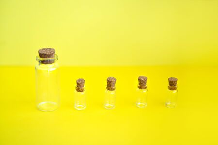 Row of multiple mini transparent glass bottles with closed brown cork lids on yellow background. Rustic and vintage jars small and clean. Old medicin keepings.の写真素材