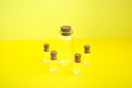 Multiple mini transparent glass bottles with closed brown cork lids on yellow background. Rustic and...
