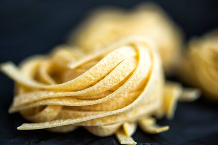 Macro picture of traditional Italian raw uncooked pasta Tagliatelle, selective focus. Vegetarian...