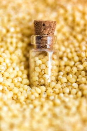 Vertical picture with soft focus of tiny corked glass jar with millet on background from millet, top view. Concept of healthy nutrition, diet, vegetarian products. Nutrition concept. Selective focus.の写真素材