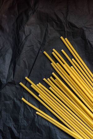Vertical picture of bunch of raw dry uncooked pasta spaghetti lay on black crumpled paper background. Selective focus. Vegetarian food. Nutrition concept. Italian kitchen. Food preparation.の写真素材