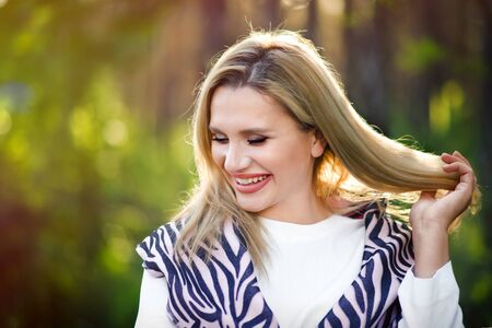 Portrait of smiling happy beautiful blonde 30 years old woman touching hair and laughing with closed eyes in forest. Freedom, happines, close to nature. Outdoors photoshoot of young sexy girl.の写真素材