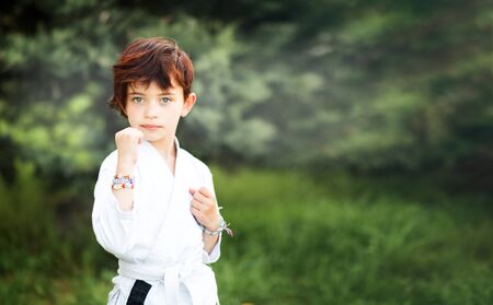 Portrait of short haired 7 years old girl in white kimono making karate kata training outdoors. Martial arts. Sport and activity for children. Japanese combat. Space for text on the right.の写真素材