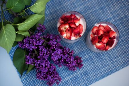 Layered strawberry homemade italian creamy dessert panna cotta with fresh berries in glass on blue background with branch of fresh purple lilac. Organic sweet. Top view of strawberry panna-cotta.の写真素材