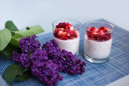 Layered strawberry homemade italian creamy dessert panna cotta with fresh berries in glass on blue background with branch of purple lilac. Organic sweet. Side view of strawberry panna-cotta.の写真素材