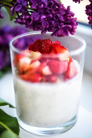 Vertical close-up picture of layered strawberry homemade italian creamy dessert panna cotta with fresh berries in glass with branch of purple lilac. Organic sweet. Side view of strawberry panna-cotta.の写真素材