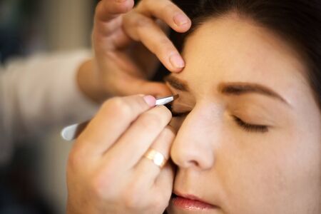 Close-up backstage scene: professional make-up artist doing eyebrow correction. Makeup artist...