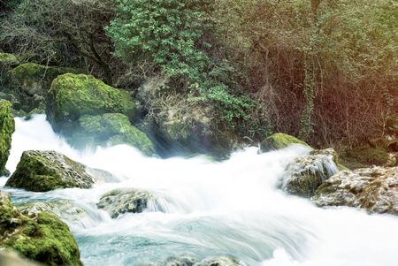 Rough mountain river with white foam, very cold and transparent, close-up. Ecologically clean water. Green wet stones and rapid stream in spring sunny day. River Sorgue in Provence, France.の写真素材