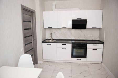 Modern kitchen interior with white dining table, white chairs, oven, sink and range hood . Modern design of black and white kitchen, straight view.の写真素材