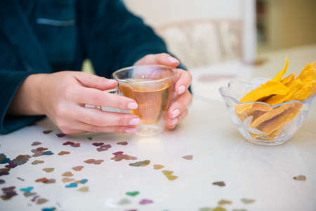 Hands of a girl holding a transparent cup with green tea sitting near table. Bright highlights on a glass. Cozy picture. Mango pieces like healthy dessert. Close up. Organic healthcare.の写真素材