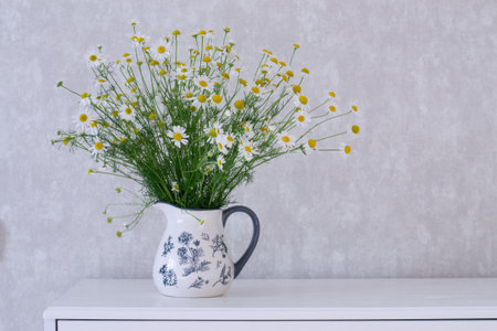 Beautiful bouquet of chamomile flowers in a vase on a white tableの写真素材