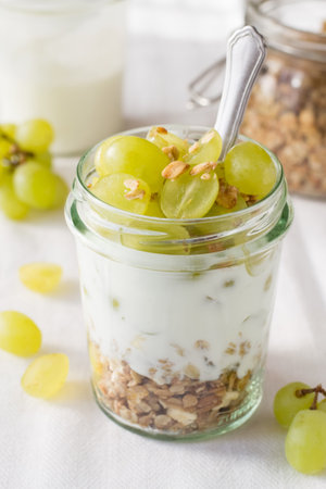 Granola with yogurt and grapes in a glass jar, verticalの写真素材
