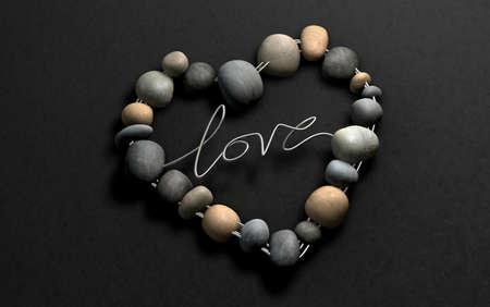 A handcrafted heart shape made out of wire and stones with the word  Love spelt out on a stone backgroundの写真素材