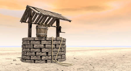A brick water well with a wooden roof and bucket attached to a rope in a flat barren landscape with an orange skyの写真素材