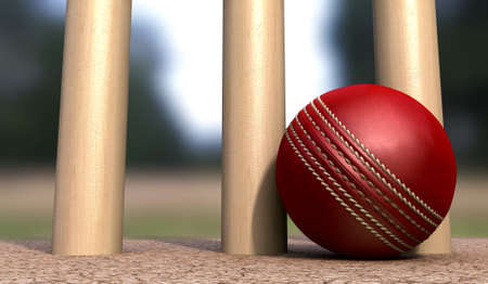 A red leather cricket ball lying on cracked soil at the base of wooden cricket wickets in the...