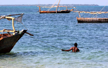 A traditional dhow sail boat on emerald blue water alongside a sandy white beach in Zanzibar