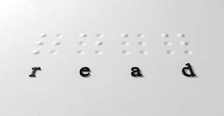 A closeup concept of a set of four isolated braille letters spelling out the word read and extruded regular black letters corresponding on a textured white paperの写真素材