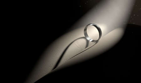 A single spotlight shining on a ring on a book castng a heart shaped shadow on a dark backgroundの写真素材
